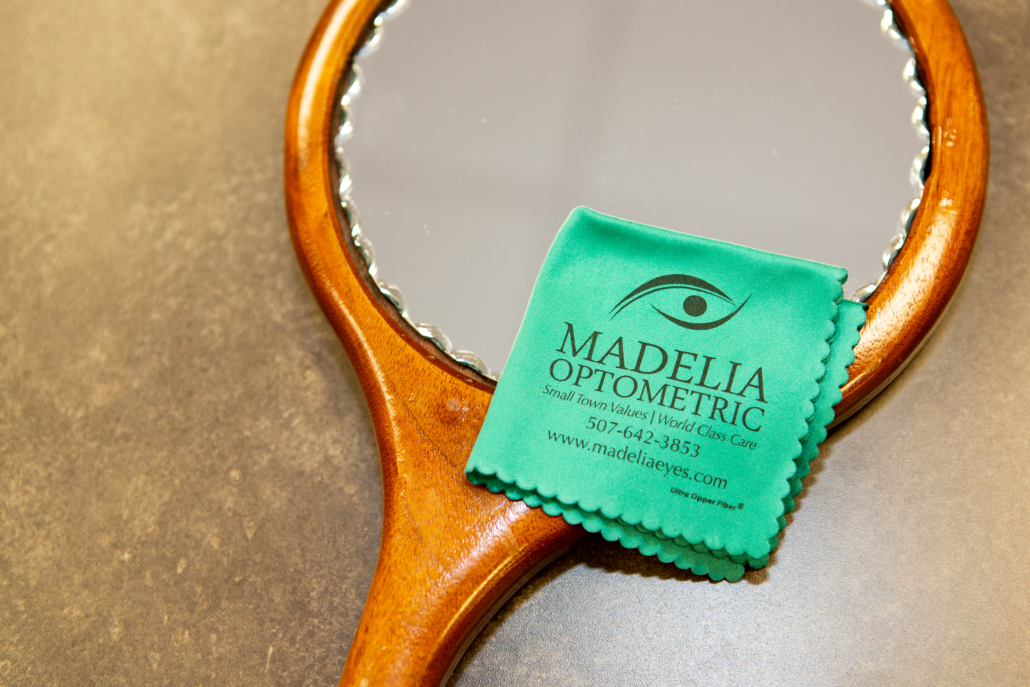 Hand mirror and lens cleaning cloth with Madelia Optometric on it